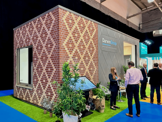 The outside of the Bedroom Evolved module, in situ on the conference fall. The left had side is finished with brick slips in a diamond pattern, with a complementary diamond pattern to the right hand side, but using grey cladding.