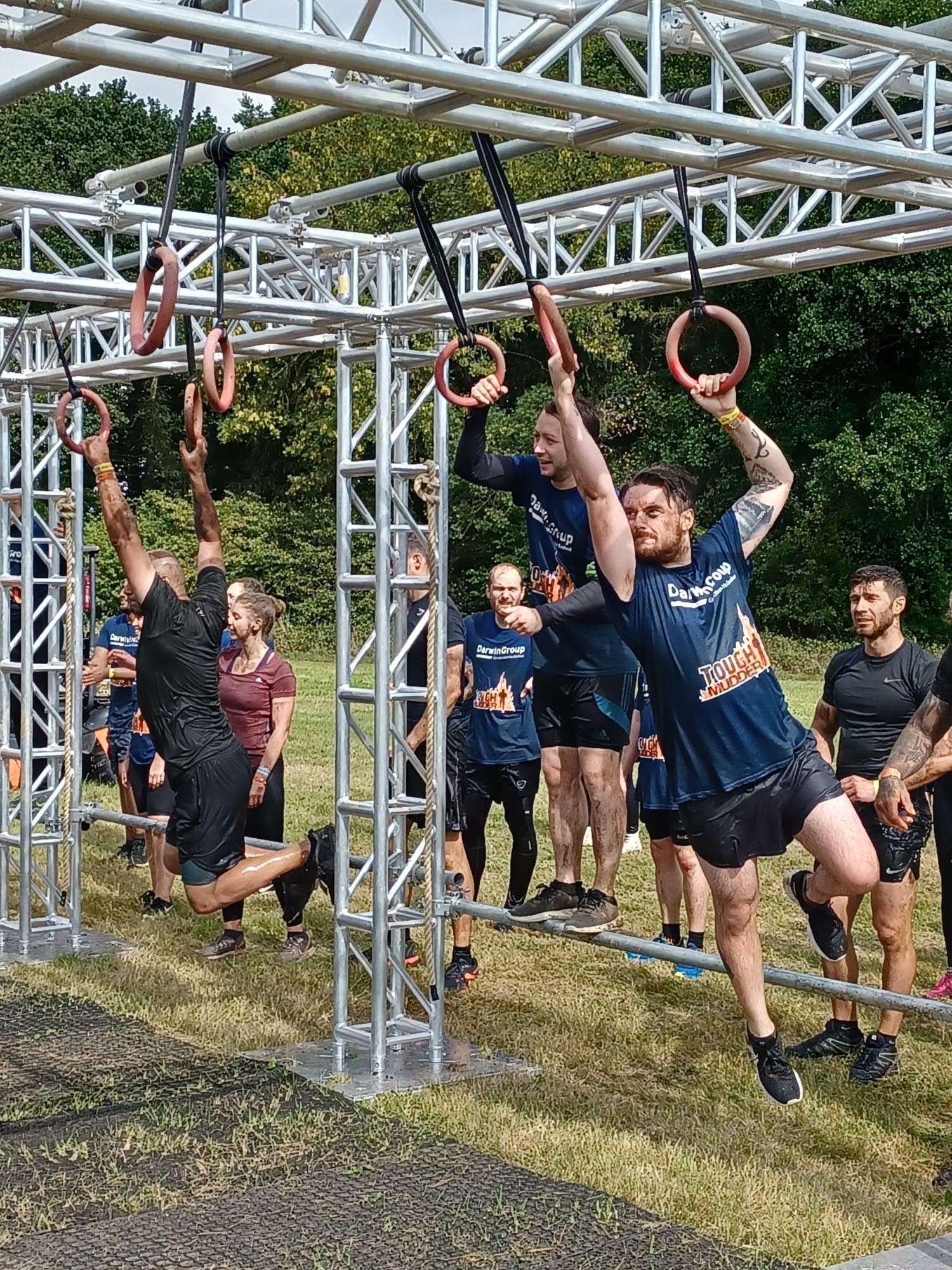 A 'hang tough' obstacle from the course. People are queueing to take part while three people are swinging from one hoop to the next.