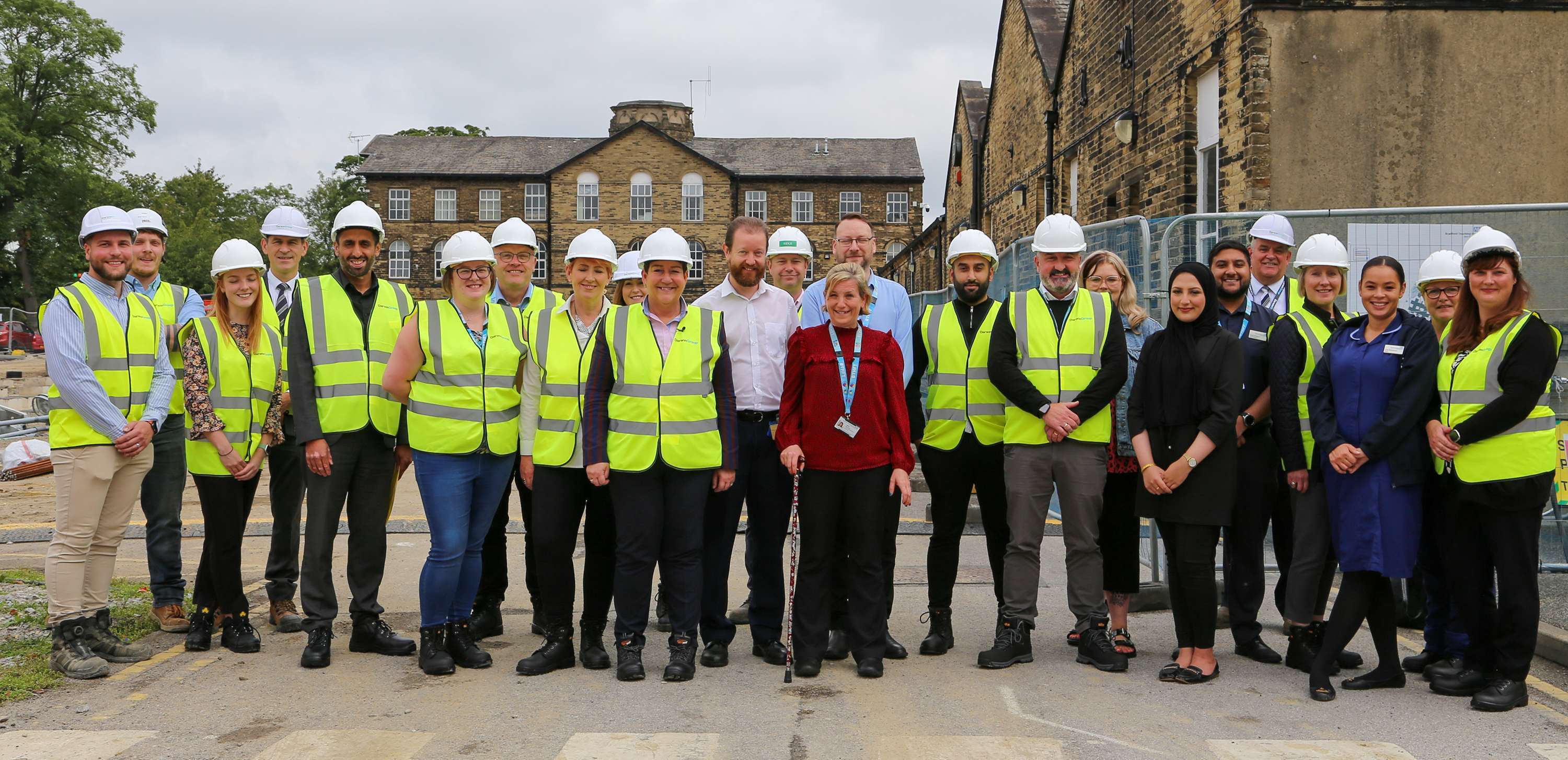 Group photo of the NHS Trust team, all wearing hi-vis and hard hats, on the site which will soon house the new Day Case Unit.