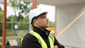 A man looks up at a newly installed steel framed module. He is wearing a hard hat and high-vis vest.