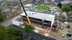 A bird's eye view of a construction site during module install. In the foreground, a large crane is lifting a module into position.