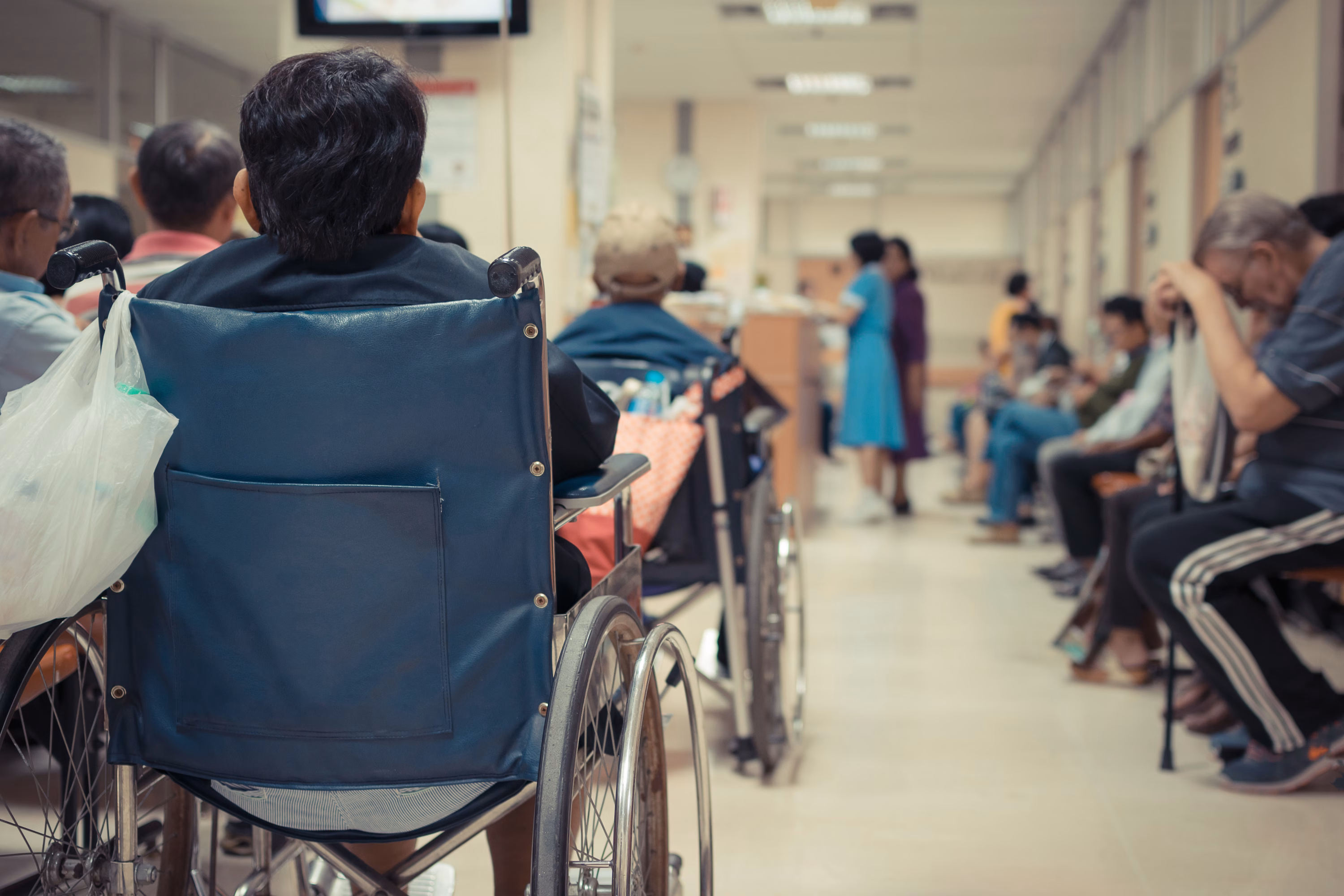 A waiting room in a medical centre. The photo shows lots of people sat in chairs with their backs to the camera.