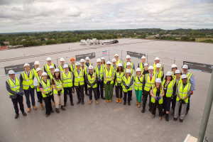 A group of people, photographed from in front and above. They are stood on the flat roof of the Coast building. They are all wearing high-vis vests, hard hats and safety gloves.