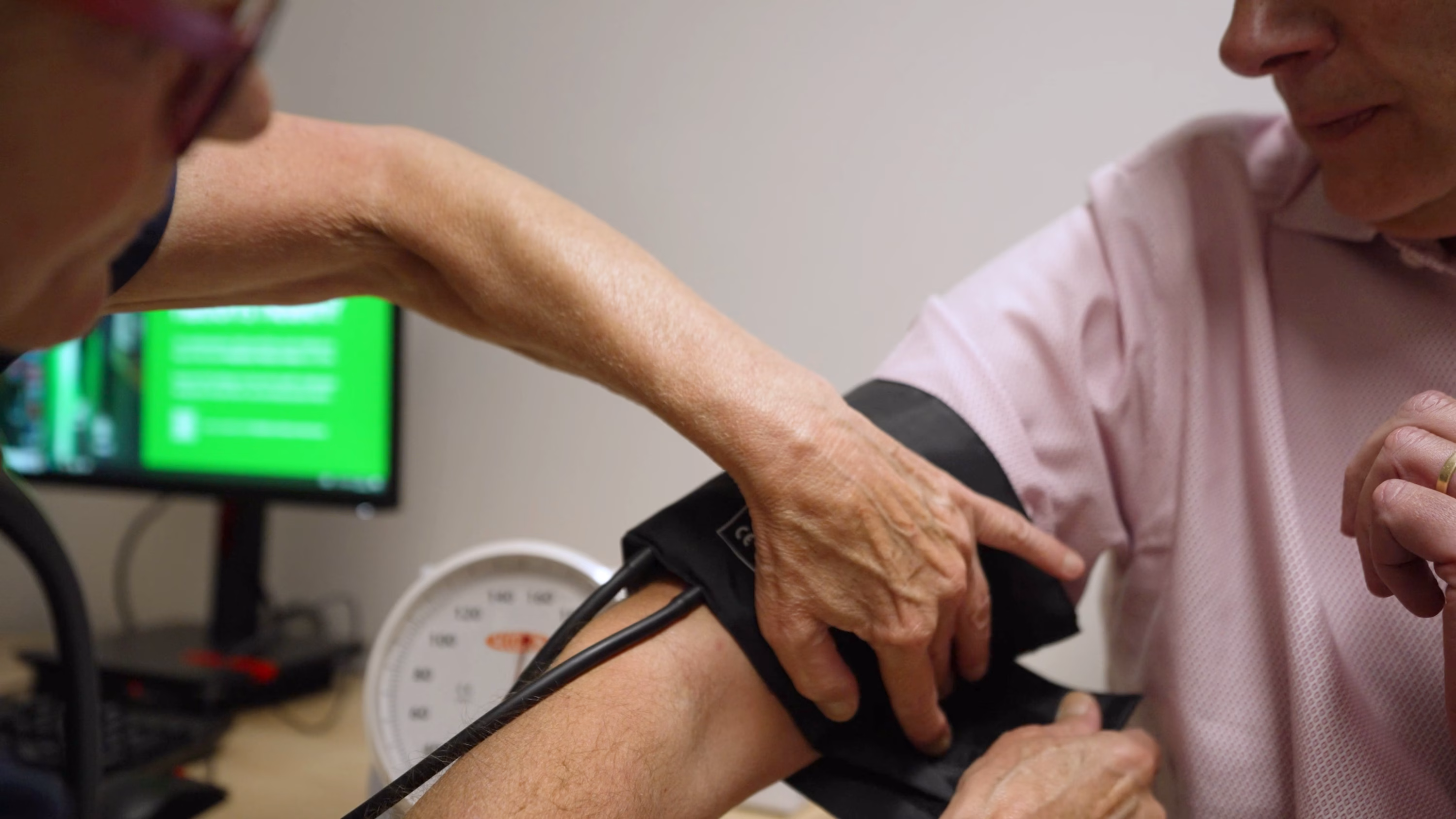 A GP is taking the blood pressure of a patient. The image is a close up of their arms.