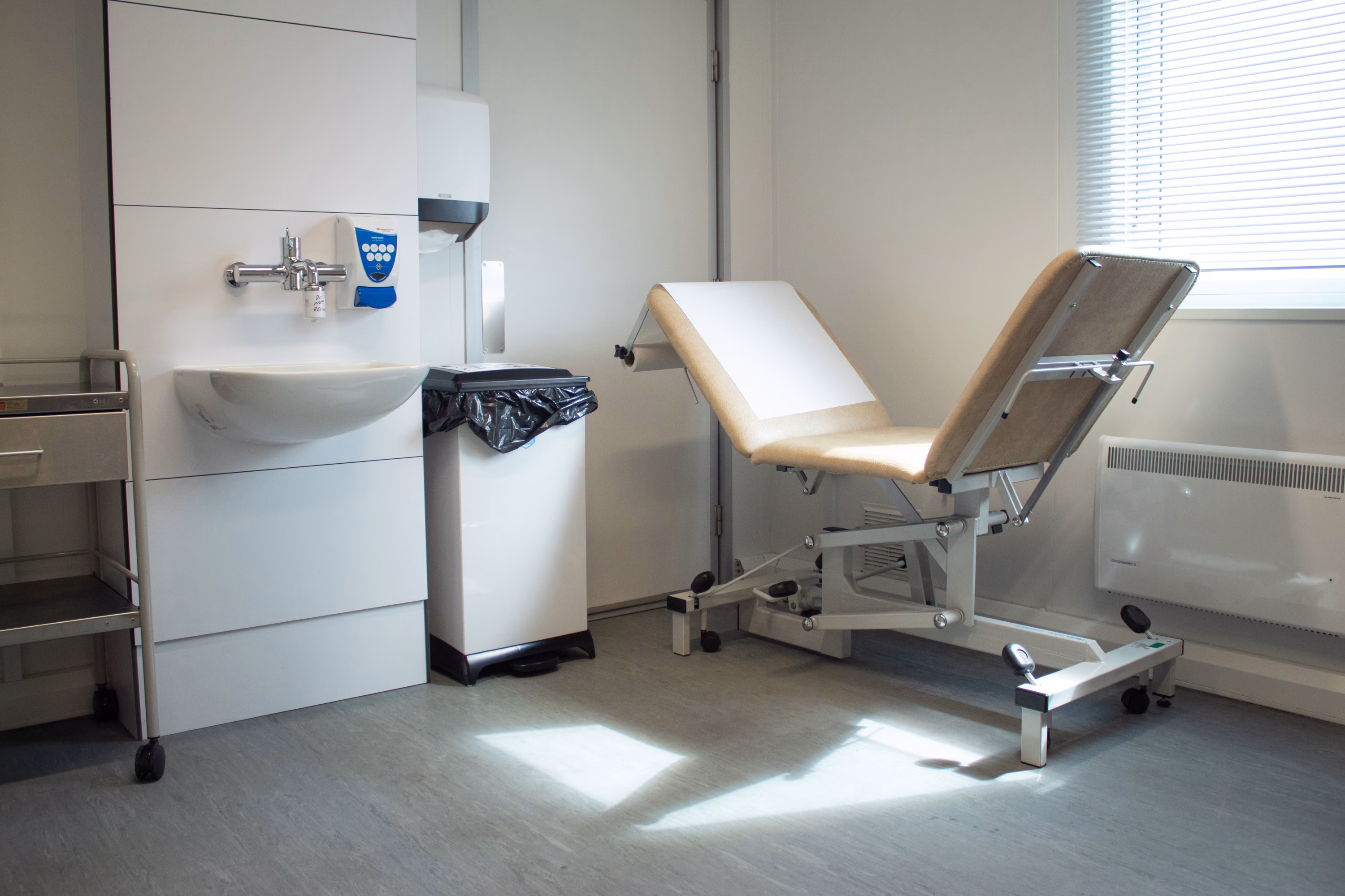 Healthcare consultation room showing bed and IPS sink with light coming from window