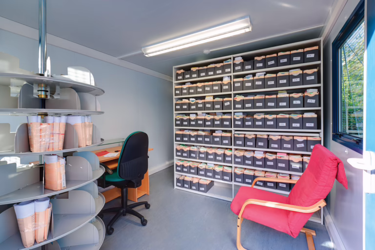 Inside a storage space at a GP surgery. There are many shelves full of papers, sorted into trays.